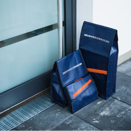 Zwei blaue Boomerang Mehrwegversandtaschen stehen vor einer Haustür